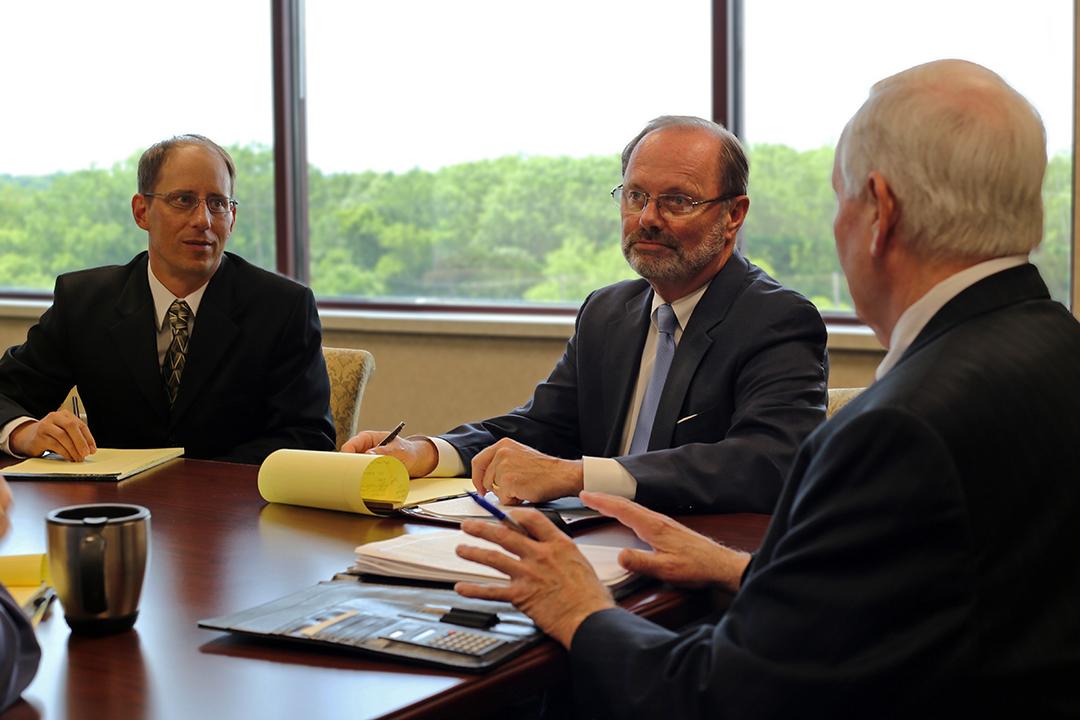 Three men in suits seated at a conference table, engaged in discussion during a business meeting