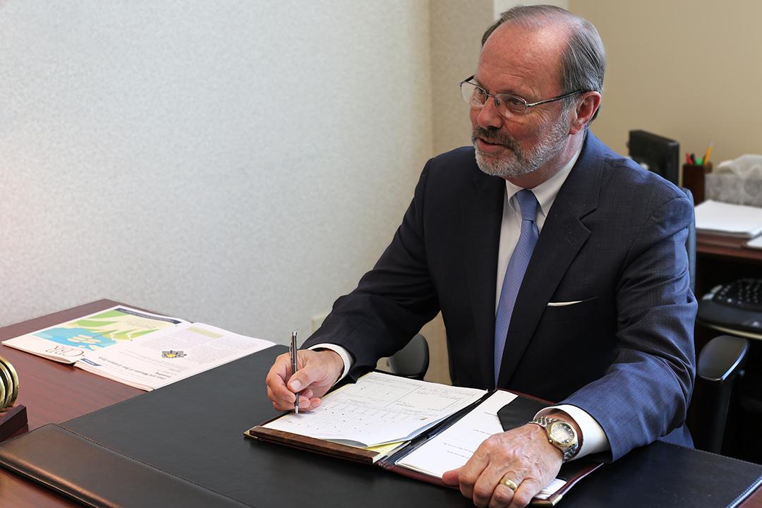 A man in a suit and tie seated at a desk, focused on his work with a professional demeanor.